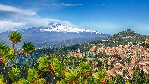 Roofs of a lot of buldings. Smoking snow-capped Mount Etna volcano. Taormina, Sicily, Italy